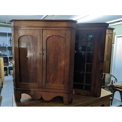 363 - A Georgian mahogany veneered corner cabinet, internal shelves on a base with twin arched doors on br... 