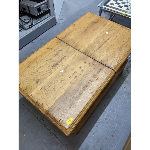 182 - A solid oak coffee table with a double opening hinged to providing storage inside, measuring 106cm x... 