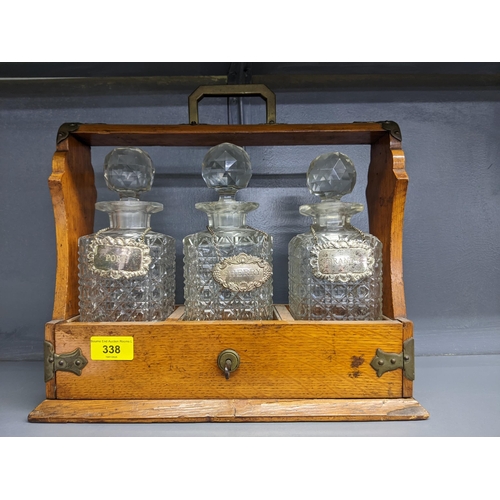 338 - An early 20th century oak Tantalus with three cut crystal decanters and silver plated decanter label... 