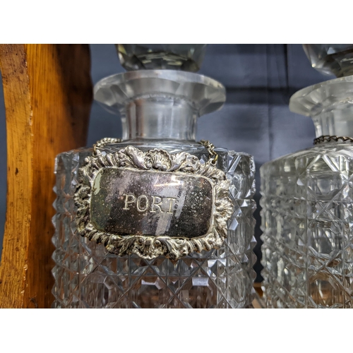 338 - An early 20th century oak Tantalus with three cut crystal decanters and silver plated decanter label... 