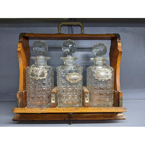 338 - An early 20th century oak Tantalus with three cut crystal decanters and silver plated decanter label... 