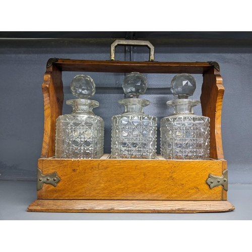 338 - An early 20th century oak Tantalus with three cut crystal decanters and silver plated decanter label... 