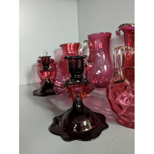 452 - A collection of cranberry coloured glass to include two candlesticks, two jugs, a vase and other ite... 