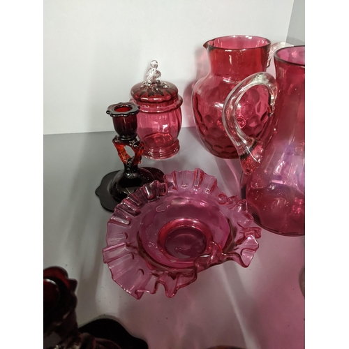 452 - A collection of cranberry coloured glass to include two candlesticks, two jugs, a vase and other ite... 