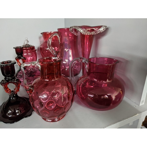 452 - A collection of cranberry coloured glass to include two candlesticks, two jugs, a vase and other ite... 