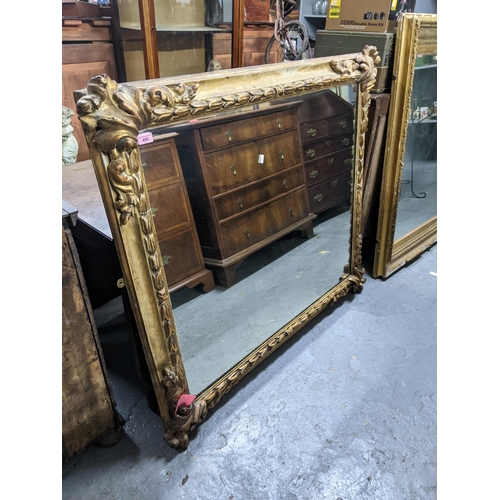 495 - A large gold coloured moulded mirror decorated with motifs in each corner with a repeating symmetric... 