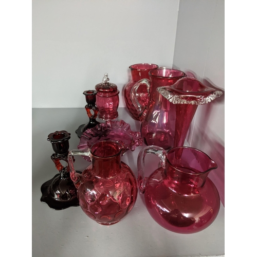 452 - A collection of cranberry coloured glass to include two candlesticks, two jugs, a vase and other ite... 