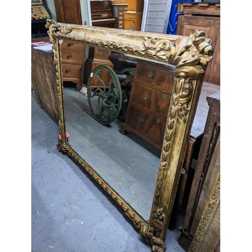 495 - A large gold coloured moulded mirror decorated with motifs in each corner with a repeating symmetric... 