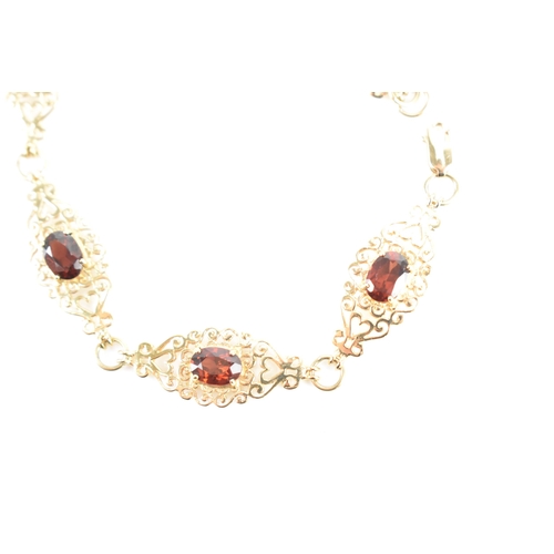 219 - A garnet 9ct gold bracelet, having six filigree panels with heart and scrolls, each inset with oval ... 