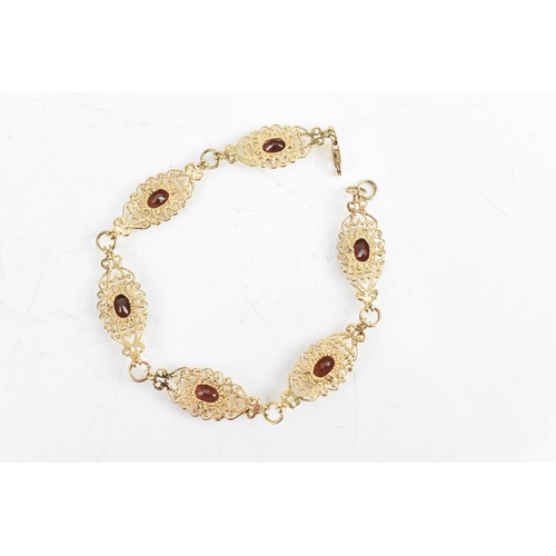 219 - A garnet 9ct gold bracelet, having six filigree panels with heart and scrolls, each inset with oval ... 