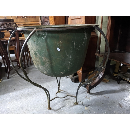 480 - A weathered metal garden planter in a wrought iron stands, 75cm high x 51cm internal diameter, along... 