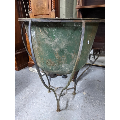 480 - A weathered metal garden planter in a wrought iron stands, 75cm high x 51cm internal diameter, along... 