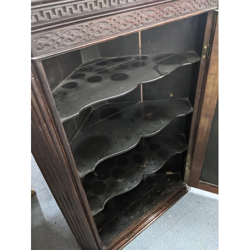 73 - A late 19th/early 20th century hanging oak corner cupboard with an ornate frieze, panelled door and ... 