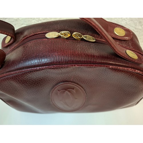 14 - Must de Cartier- A late 20th Century burgundy leather handbag in the bowling bag style having gold t... 