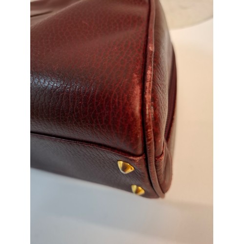 14 - Must de Cartier- A late 20th Century burgundy leather handbag in the bowling bag style having gold t... 