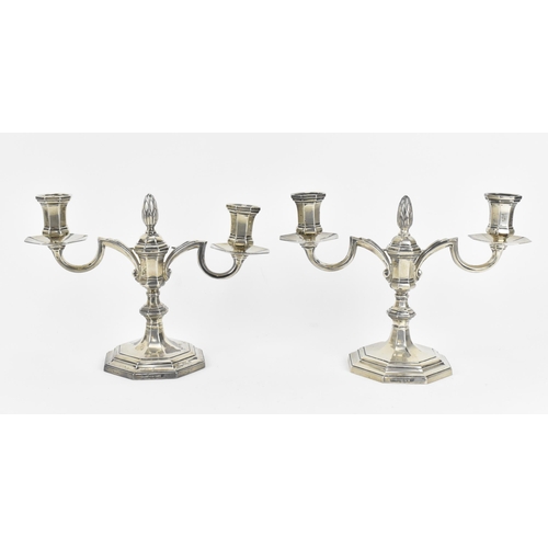 A pair of Elizabeth II silver twin-light candelabra by Mappin & Webb, Sheffield 1956, of faceted design with central pineapple finial, on a knopped stem with spreading and stepped octagonal base, 18 cm high, combined weight 1100 grams