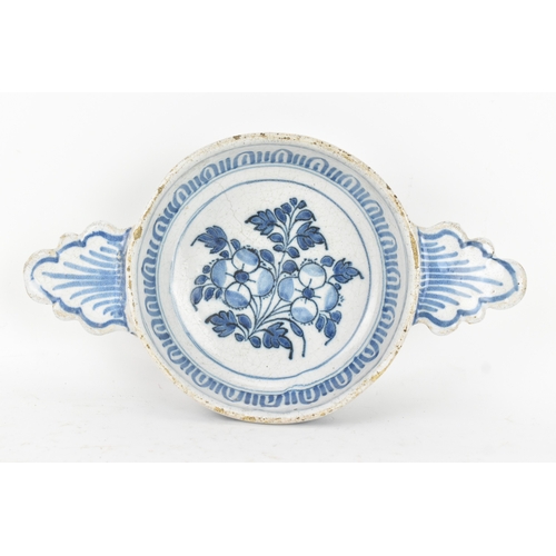 185 - An 18th century Delft faience porringer, painted in underglaze blue with flowering branches and foli... 