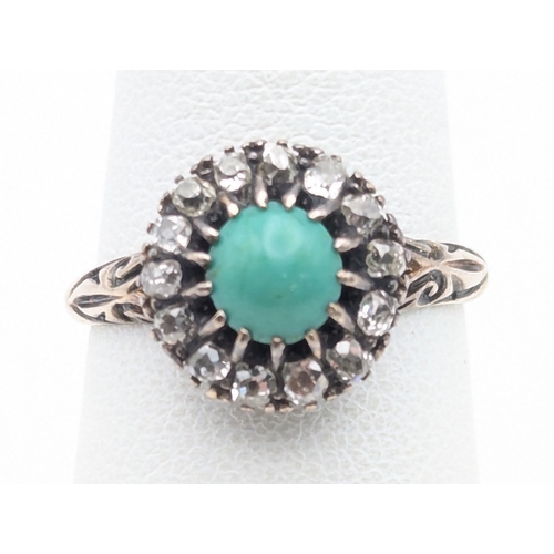 94 - A diamond and turquoise halo ring with a central turquoise in a white metal claw setting, on a yello... 