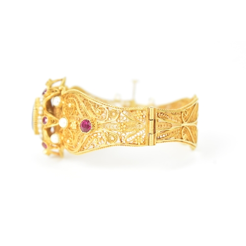 2 - An 18ct gold filigree sapphire, ruby and pearl bracelet, the ornate hinged panels decorated with scr... 
