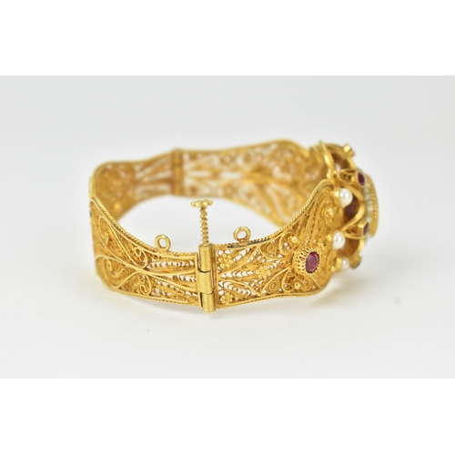 2 - An 18ct gold filigree sapphire, ruby and pearl bracelet, the ornate hinged panels decorated with scr... 