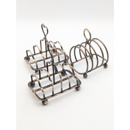 27 - Three silver toast racks to include a pair of Edwardian examples on four ball feet with heart shaped... 