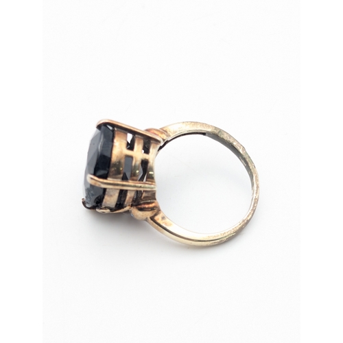 56 - A yellow metal ring tested as 9ct with a claw set oval fasted cut dark stone possibly topaz or zirco... 