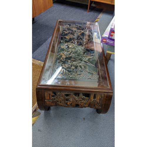 29 - A Chinese carved low table the top depicting a scene of warriors and with a glass top 38cm h x 110.5... 