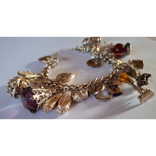 35 - A silver charm bracelet with multiple charms to include silver, glass and enamel charms, total weigh... 