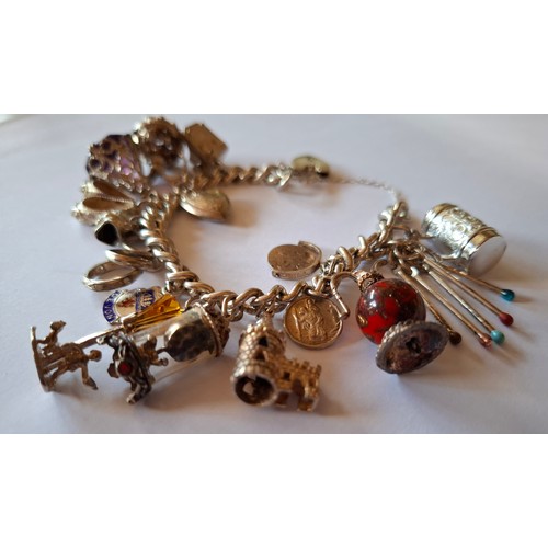 35 - A silver charm bracelet with multiple charms to include silver, glass and enamel charms, total weigh... 