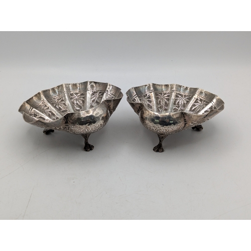 49 - A pair of white metal Indian shell shaped bonbon dishes with embossed and engraved decoration depict... 
