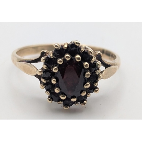 27 - A 9ct yellow gold garnet set cluster ring featuring a faceted cut oval garnet to the centre surround... 