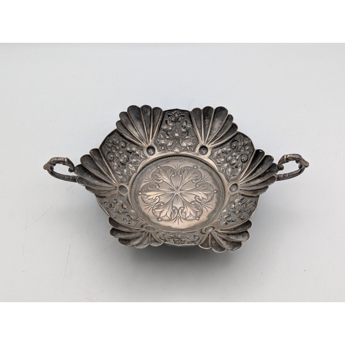 55 - A silver bon bon dish in hexagonal form, shell shaped and floral embossed panels and scalloped borde... 