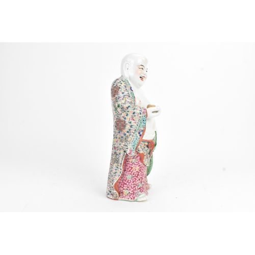 15 - A Chinese famille rose porcelain figure of Buddha, modelled standing holding a cup, his robe decorat... 