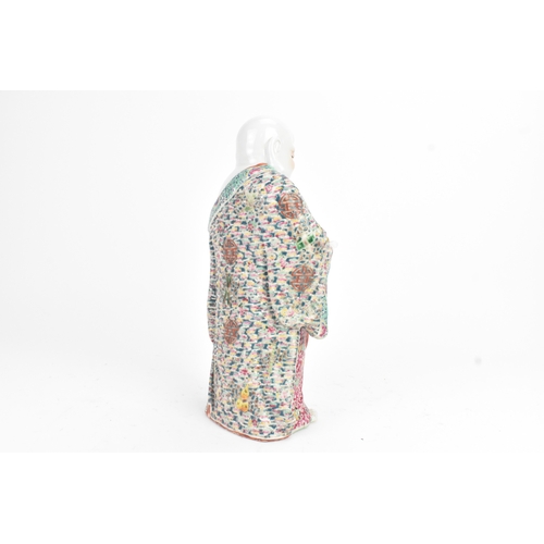 15 - A Chinese famille rose porcelain figure of Buddha, modelled standing holding a cup, his robe decorat... 