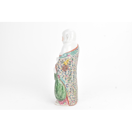 15 - A Chinese famille rose porcelain figure of Buddha, modelled standing holding a cup, his robe decorat... 