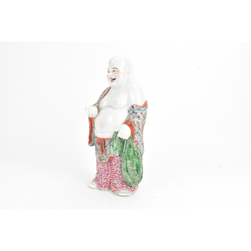 15 - A Chinese famille rose porcelain figure of Buddha, modelled standing holding a cup, his robe decorat... 