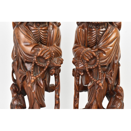 36 - A pair of Chinese hardwood carved figures of immortals, 20th century, each modelled standing holding... 