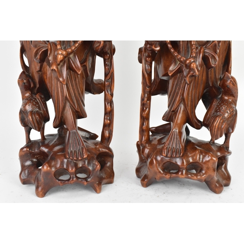 36 - A pair of Chinese hardwood carved figures of immortals, 20th century, each modelled standing holding... 