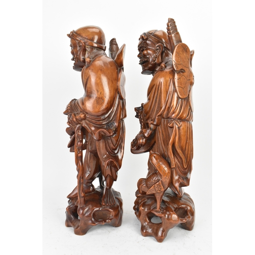 36 - A pair of Chinese hardwood carved figures of immortals, 20th century, each modelled standing holding... 