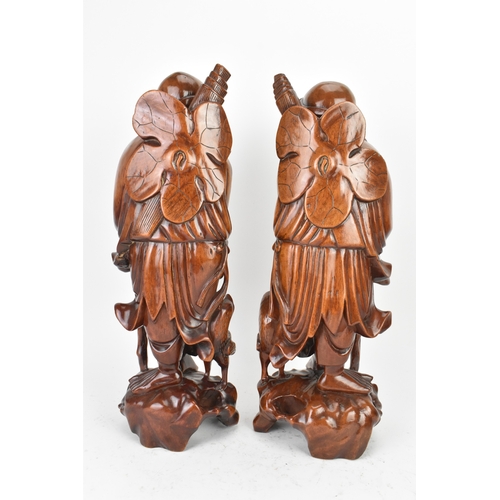 36 - A pair of Chinese hardwood carved figures of immortals, 20th century, each modelled standing holding... 