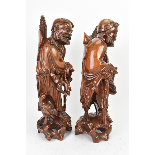 36 - A pair of Chinese hardwood carved figures of immortals, 20th century, each modelled standing holding... 
