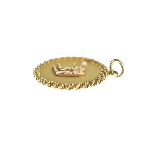 31 - A 9ct yellow gold pendant, featuring an engine turned ground, with inset pearl, decorated with two f... 