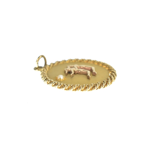 31 - A 9ct yellow gold pendant, featuring an engine turned ground, with inset pearl, decorated with two f... 