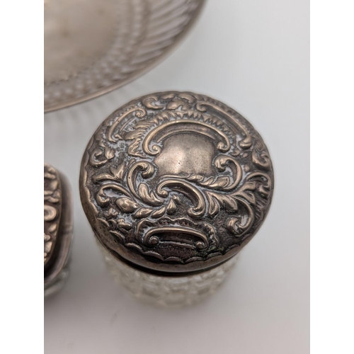 59 - A white metal dish having repeating pierced decoration, together with two silver topped dressing tab... 