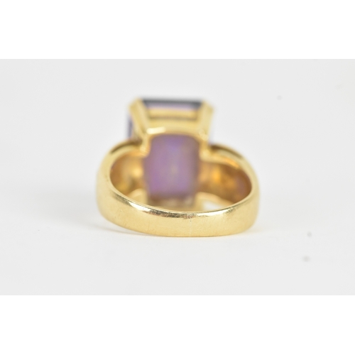 23 - An amethyst 18ct gold dress ring, the emerald cut amethyst in a four claw setting measuring approxim... 