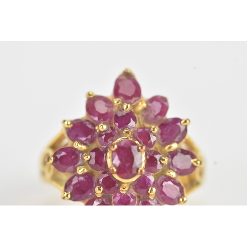29 - A ruby 18ct yellow gold cluster dress ring, of radiating flower head design, set with twenty-one rub... 
