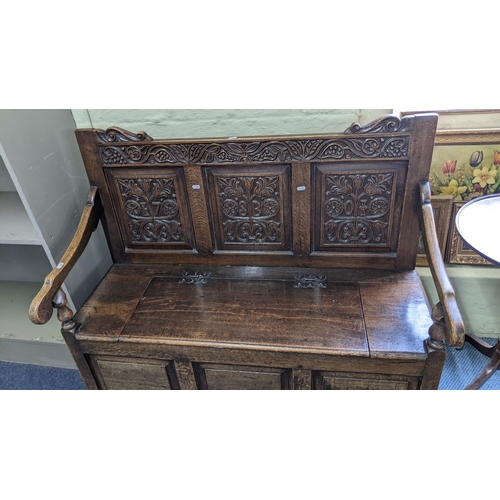 8 - An early 20th century oak settle having a carved panelled back, hinged seat and on block feet. 97H x... 