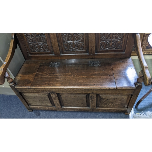 8 - An early 20th century oak settle having a carved panelled back, hinged seat and on block feet. 97H x... 