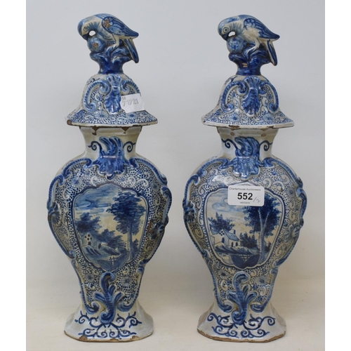 552 - A pair of Dutch Delft vases, the covers with bird finials, the bases decorated dwellings, 34 cm high... 