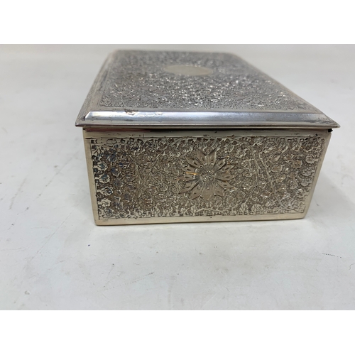 28 - A Persian silver coloured metal table cigarette box, decorated flowers and foliage, 13.5 cm wide